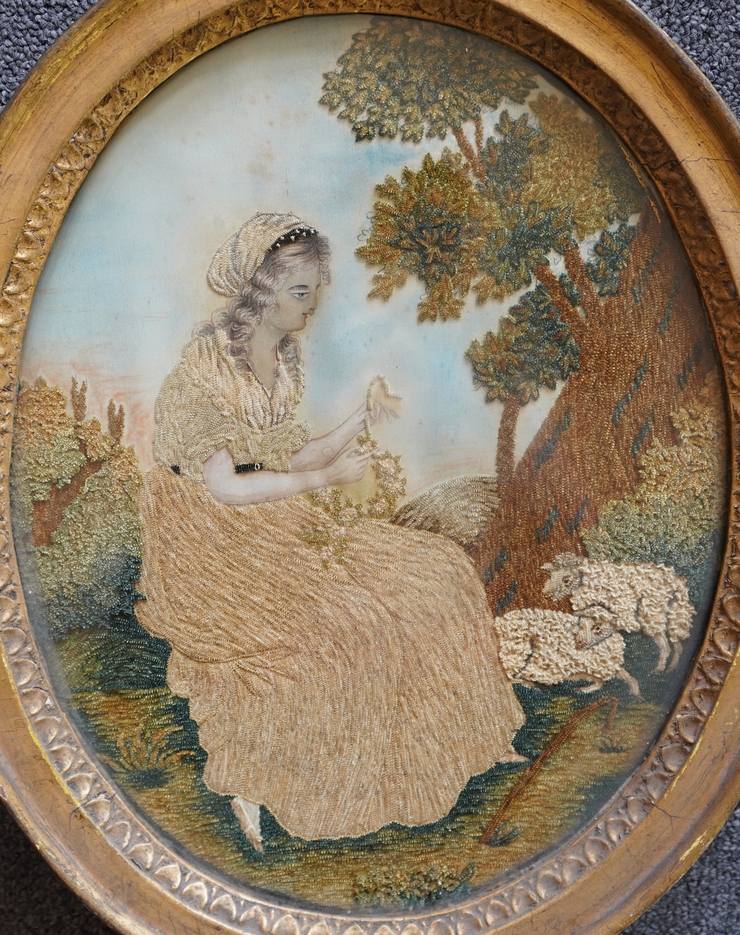 A pair of unusual early 19th century oval silk Chenille embroideries, one depicting a seated lady surrounded by a lion and donkey, the other depicting a seated shepherdess under tree with two sheep. Both have water colou